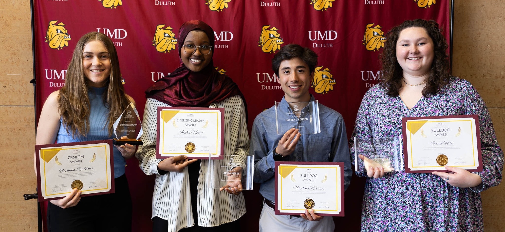 2024 Student Award Winners - Picture of 4 students hold their awards and certificates in front of a UMD backdrop